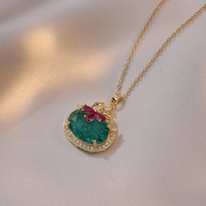 Collier doré élégant avec pierre verte et détails floraux rouges sur fond de soie