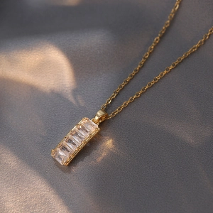 Elegant gold necklace with baguette-cut zircon pendant on grey silk background