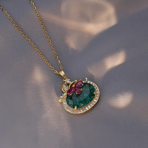 Collier en or avec pierre ovale verte et détails rouges sur un fond de soie grise