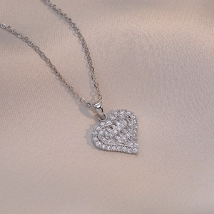 Silver heart pendant necklace with zircon stones on champagne silk fabric background
