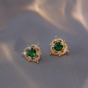 Vintage gold heart studs with green gemstone and zircon halo on textured fabric