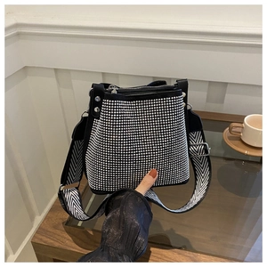 Détail d'un sac seau noir en strass avec une large bandoulière à motifs sur une table