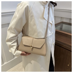 Detail of elegant beige crossbody bag with gold ring buckle on white trench coat