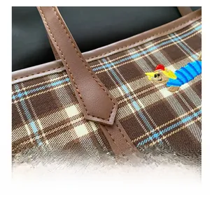 Detail of brown checkered tote bag featuring colorful cartoon embroidery and leather handle
