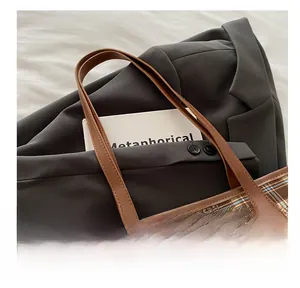 Detail of checkered tote bag featuring brown leather handles and blue caterpillar embroidery