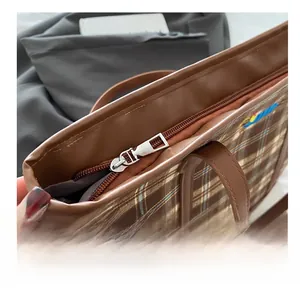 Close-up of smooth silver metal zipper on a brown plaid tote bag with leather trim
