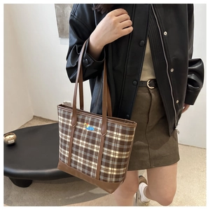 Detail of checkered tote bag with cartoon embroidery and brown leather handles on model