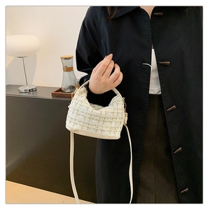 Detail of cream tweed crescent bag with leather handle and gold hardware on model