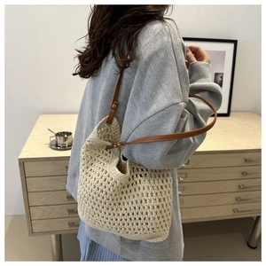 Detail of beige crochet tote bag with brown leather strap worn over a grey sweatshirt