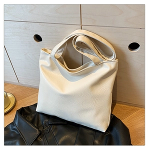 Detailed view of beige tote bag with crinkled PU leather texture against a wooden background