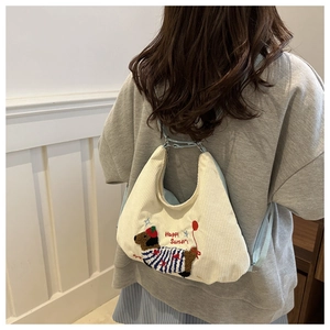Detail of dachshund embroidery on off-white corduroy shoulder bag with blue strap