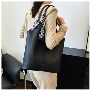Dettaglio della borsa tote in pelle nera con elegante sciarpa a scacchi sul manico