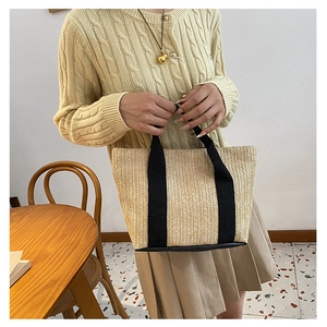 Detail of hand-woven straw tote bag with black fabric handles and sturdy black base
