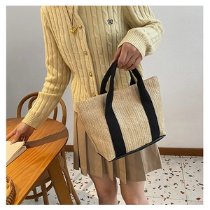 Detail of hand-woven straw tote bag with wide black canvas handles and leather trim