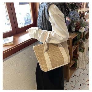 Detail of woven straw handbag with canvas handles shown in a relaxed lifestyle setting