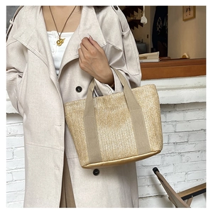 Detailed view of hand-woven straw tote bag with metallic base and khaki straps