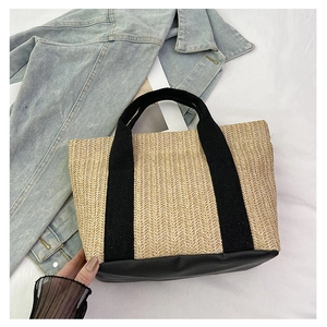 Handmade woven straw tote bag with black leather base and canvas handles on denim background