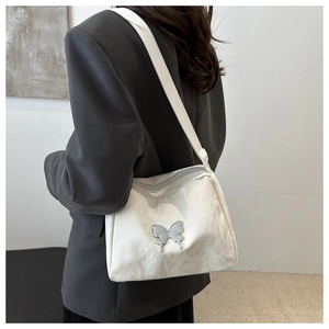 Close-up of white shoulder bag with silver butterfly hardware on a black blazer