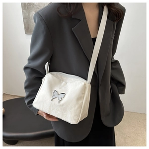 Detailed view of a white shoulder bag with pleated texture and silver butterfly buckle