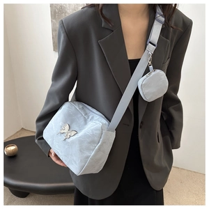 Detailed view of silver butterfly metal buckle on light blue textured crossbody bag