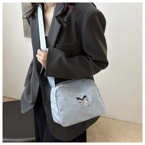 Detail of light blue wrinkled nylon crossbody bag with metal butterfly logo on grey suit