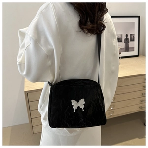 Black crinkled shoulder bag with metallic butterfly buckle shown on model's back