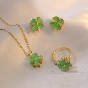 Detailset aus goldenem Kleeblatt-Schmuck mit grünen Opalsteinen auf Seidenhintergrund
