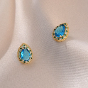 Boucles d'oreilles dorées avec pierres bleues en goutte et halo sur tissu de soie