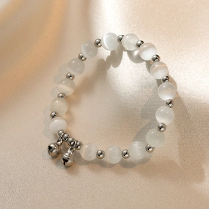 Detail of white cat eye stone beaded bracelet with silver bells on champagne satin