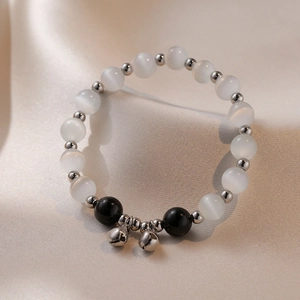 Obsidian and cat eye stone bracelet with silver bells on beige silk background