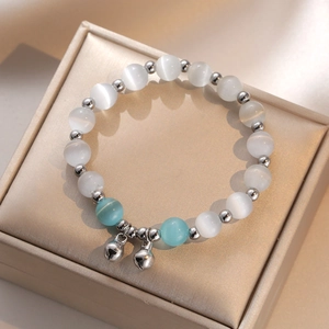 Cat's eye stone beaded bracelet with silver bell pendants on a beige jewelry display box