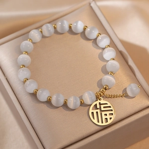 Detail of beaded bracelet with white opal stones and gold Fu character charm on jewelry box