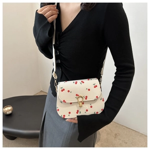Detail of cream crossbody bag with cherry print and golden metal buckle on model