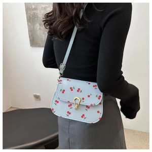 Detail of light blue saddle bag with cherry print and golden horseshoe twist lock buckle