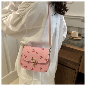 Pink crossbody bag with cherry prints and golden horseshoe lock shown on a model