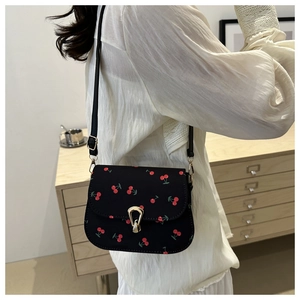 Detail of floral saddle bag with cherry print and golden horseshoe buckle on a model