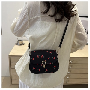 Close-up of black crossbody saddle bag with red cherry print and metal horseshoe buckle