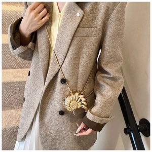 Detailed view of a golden conch shell mini crossbody bag with a fine metal chain strap
