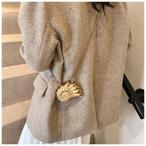 Golden shell-shaped metal crossbody bag with chain strap worn by a female model
