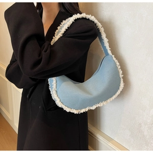 Détail du sac hobo en jean bleu clair avec franges porté sur un long manteau noir