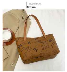 Detail of a brown leather tote bag with letter patterns and a matching shoulder strap