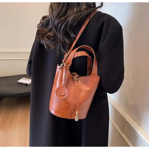 Detail view of caramel bucket bag featuring a leather smiley charm and golden lock detail