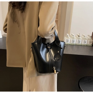 Detail of black leather bucket bag with gold lock pendant and sleek shoulder strap design