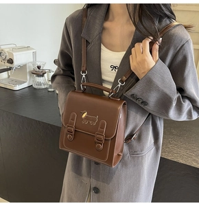 Detail of dark brown leather satchel featuring a cute puppy emblem and magnetic straps