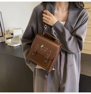 Detail of a brown leather satchel featuring a dachshund patch and retro buckle straps