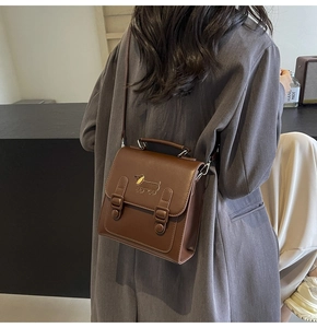 Detailed view of dark brown vintage square backpack with cute metal puppy ornament and straps