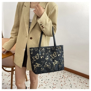 Detail of elegant black tote bag featuring gold butterfly embroidery and leather straps