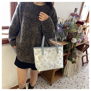 Detailed close-up of intricate gold butterfly embroidery on white jacquard tote bag