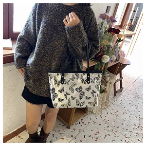 Detailed view of tote bag with butterfly print and golden rivets worn by model