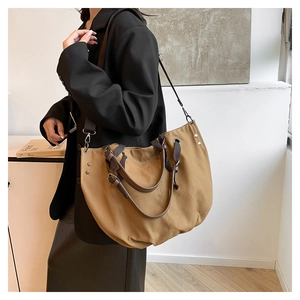 Detail of khaki canvas tote featuring brown leather handles and adjustable shoulder strap